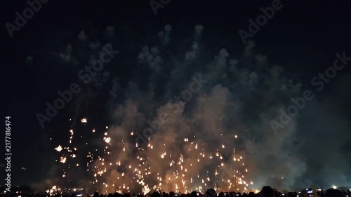 Spectacular ground-level fireworks illuminate the night sky above a large crowd of onlookers during a festive celebration.