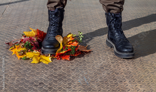 Obraz na plátně Man in black leather boots stepping on wreath of autumn leaves