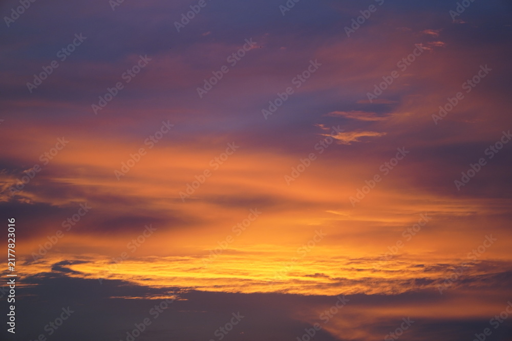 Fototapeta premium Breathtaking sunset sky with vibrant golden orange, yellow, and soft purple clouds. A peaceful natural background capturing twilight atmosphere, warm sunlight gradients, and tranquil evening beauty