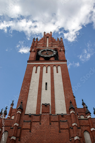 Bild auf Leinwand Historic red brick clock tower viewed from below against a bright blue sky with clouds