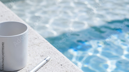 Workation by swimming pool with blank notebook and pen beside clear blue water for remote work