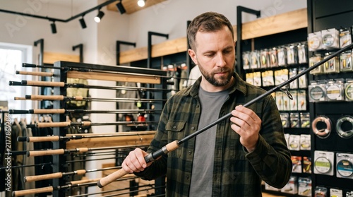 Man examining fishing rod in sporting goods store surrounded by fishing gear and equipment