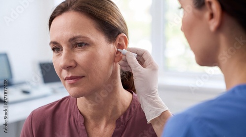 A healthcare professional carefully cleans a patient's ear with a cotton swab in a medical examination room.