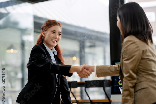 Asian businesswomen shaking hands, smiling, agreeing on a deal, forming a partnership in a modern office meeting
