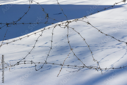 Cuadro en lienzo Sharp barbed wire strands crisscross over a frozen snowy landscape, creating a s