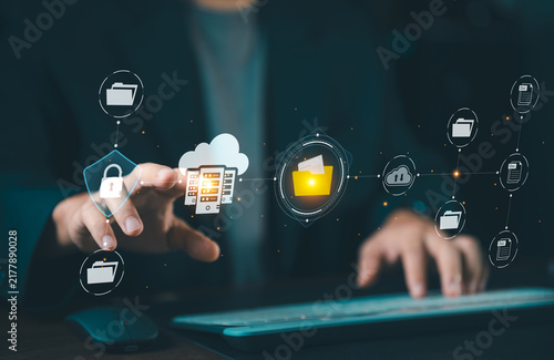 Businessman touching glowing cloud storage server hologram with secure document folders, cloud computing and data center management concept.