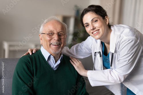 Obraz na plátně Doctor hugs happy senior man, posing for portrait during medical house call consultation