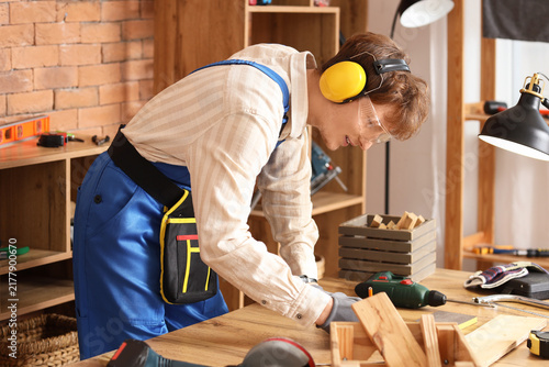 Young carpenter marking wooden plank at table in workshop