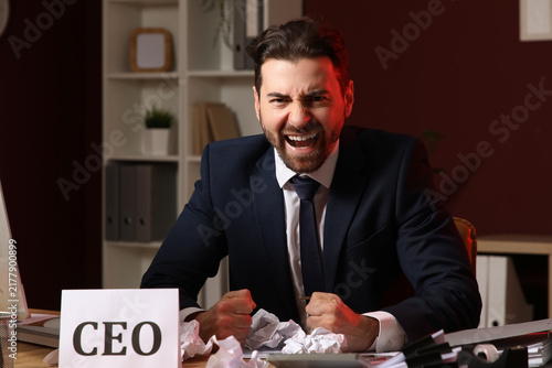 Angry businessman shouting at desk in office