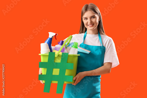 Female janitor holding bucket with cleaning supplies and hashtag sign on colo...