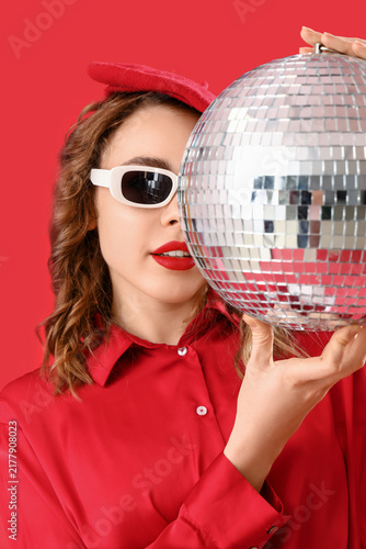 Beautiful young woman in stylish sunglasses with disco ball on red background