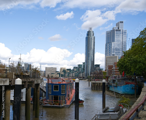 Canvas Print Colorful residential houseboats moored along the River Thames in London, England, with modern high-rise buildings and the city skyline visible in the background