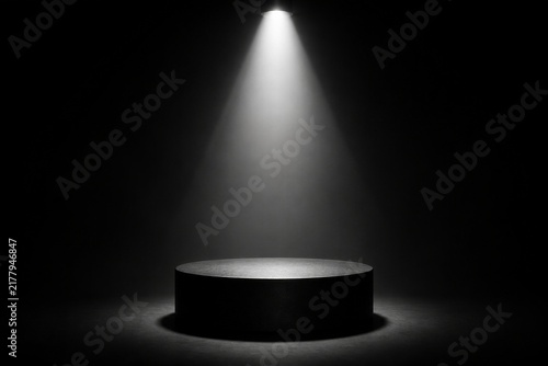 Round pedestal illuminated by single overhead spotlight in dark room