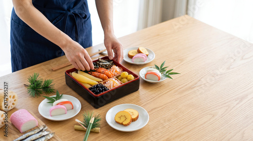Naklejka 鮮やかな海老やおめでたいおせち料理を重箱へ盛り付ける手元の和風イメージ