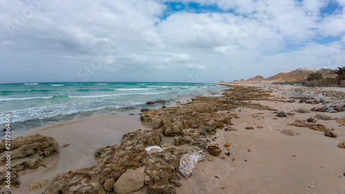 Rocky sandy beach with turquoise sea and cloudy sky
