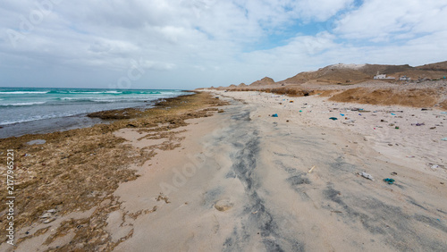 Polluted sandy beach with litter and cloudy sky