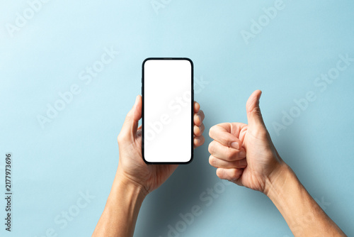 Obraz na płótnie 青い背景でスマートフォンを持ってサムズアップする男性