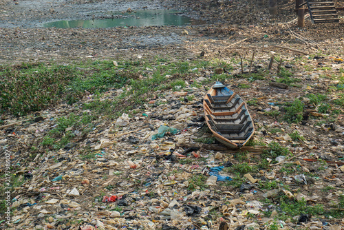 Foto A landscape photo showing a wooden boat stranded in a river covered in layers of trash and debris in a shallow, dry and murky river in the dry season