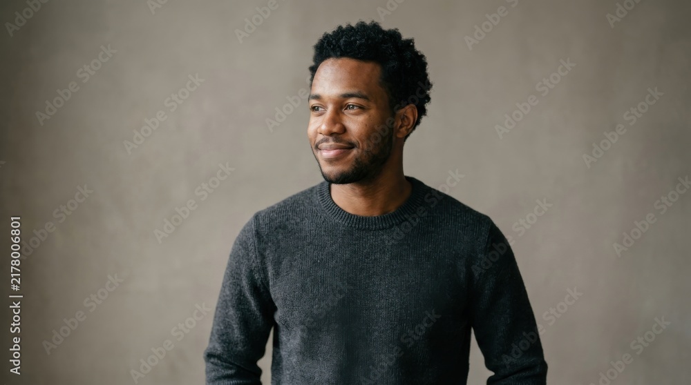 Obraz premium Confident Young African American Man Smiling Thoughtfully in Studio Setting Wearing Casual Dark Gray Sweater with Neutral Background for Commercial