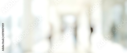 A soft-focus image depicting a blurred hallway with indistinct figures in the background, creating a sense of movement and light in an indoor space.