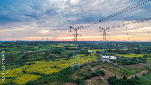 High-voltage transmission pylons stand across agricultural fields under a cloudy sunset sky, showcasing rural energy infrastructure.