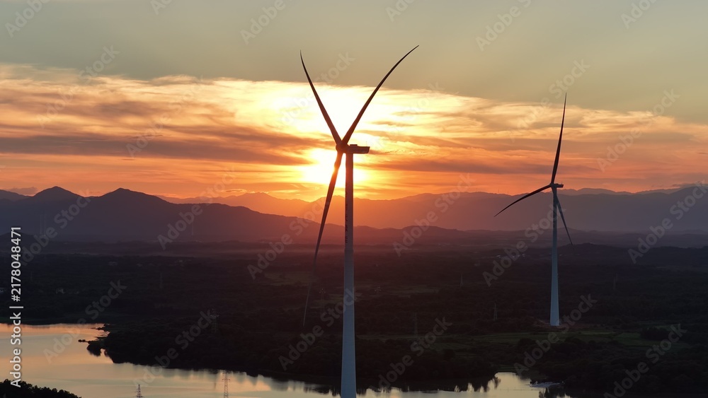 Obraz premium Wind turbines silhouetted against sunset sky over water
