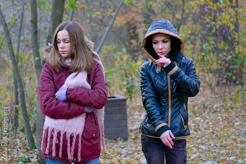 Two serious sad young women girlfriends walking in autumn forest