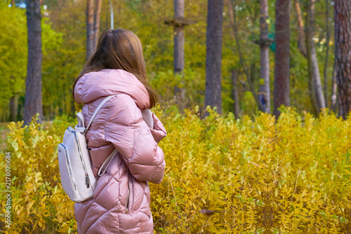 Nice woman in pink jacket with backpack walking in an autumn park