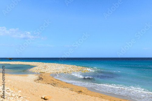 Fotografie A tranquil scene unfolds with a sandy shore meeting a rocky coastline and the va