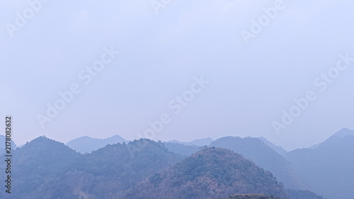 Panoramic view of hazy blue mountain ranges under a clear soft sky in a misty morning atmosphere.