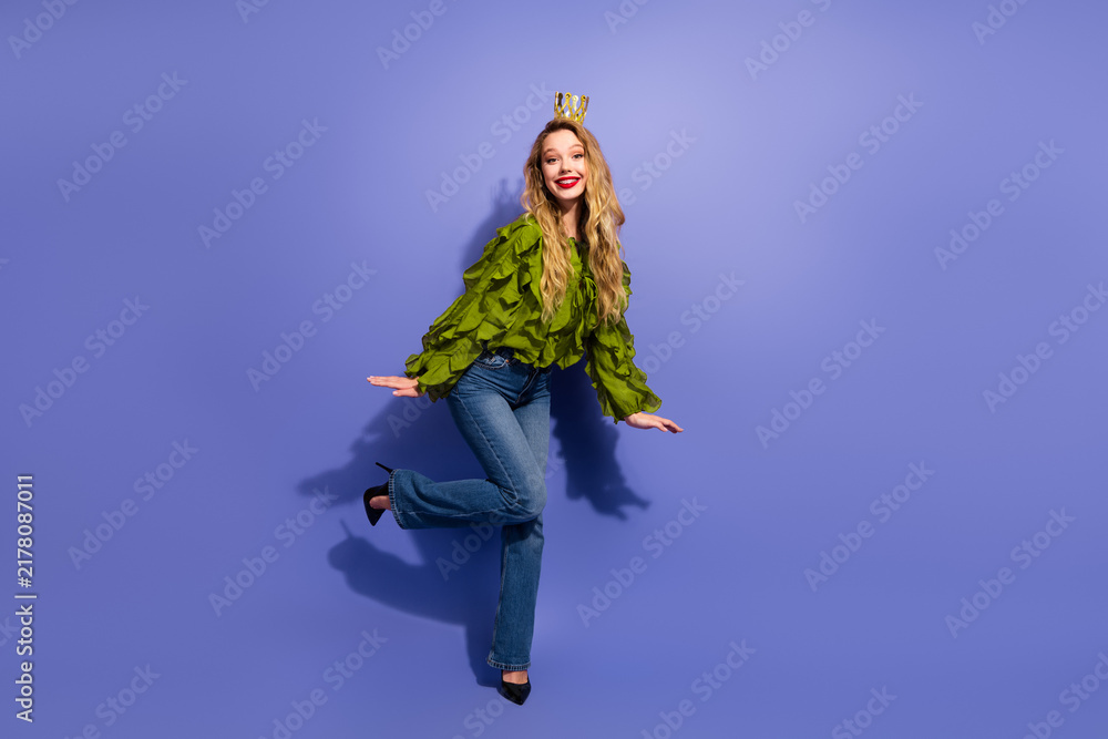 Obraz premium Charming young female model poses in green ruffled blouse and jeans with crown against purple background