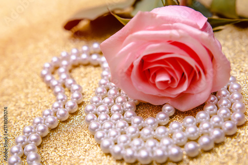 Pink rose and pearl necklace on a shiny gold background
