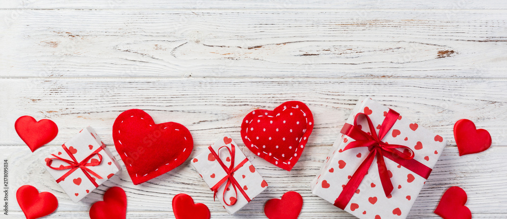 Fototapeta premium Valentine or other holiday handmade present in paper with red hearts and gifts box in holiday wrapper. Present box of gift on white wooden table top view with copy space, empty space for design