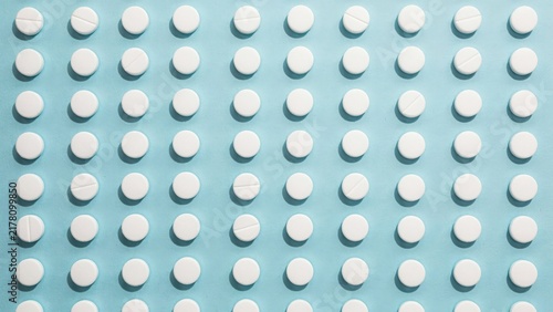 Neat uniform grid of round white pills on light blue surface, top view pharmaceutical arrangement concept, medicine