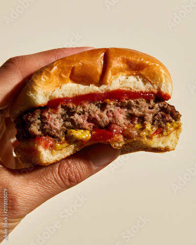 Classic Junior Burger Cut in Half with Ketchup and Mustard Shown in Hand, Highlighting Juicy Texture and Flavor