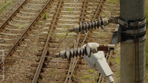 Electric wires and current dividers are shown above the railway tracks during the day. The setup highlights the infrastructure used for train operations.