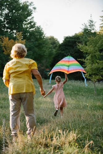 Grandmother holding granddaughter's hand, flying kite in park