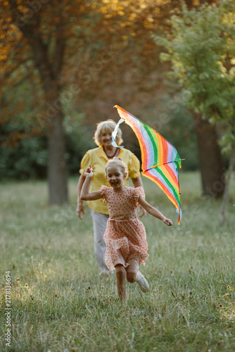 Happy granddaughter playing with kite, grandmother watching in park