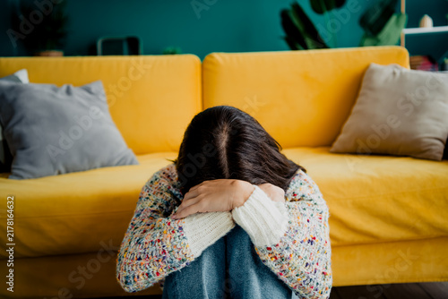 Quadro su tela Young woman sitting on the floor with head in hands leaning against a yellow sof