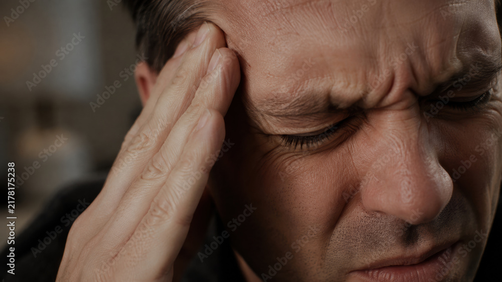 Fototapeta premium Close-up of a man hand pressing firmly against their temple, eyes squeezed shut and brow deeply furrowed in visible pain. Acute migraine pain concept