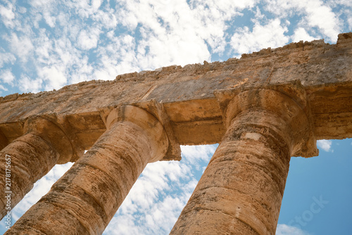 Dynamic low-angle view of Doric columns and architrave against blue sky with clouds in Segesta, Sicily, Italy