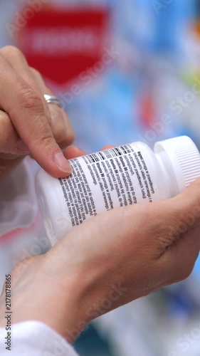 Pharmacist wearing a white coat attentively reads the instructions and ingredients on a white pill bottle label, carefully checking the dosage information before dispensing the medication