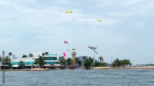4K boat perspective showing multiple giant inflatable kites hovering near the lighthouse and beach of Cartagena, Colombia.