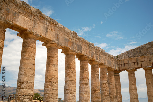 Low-angle horizontal view of interior Doric colonnade meeting corner entablature under blue sky in Segesta, Sicily, Italy