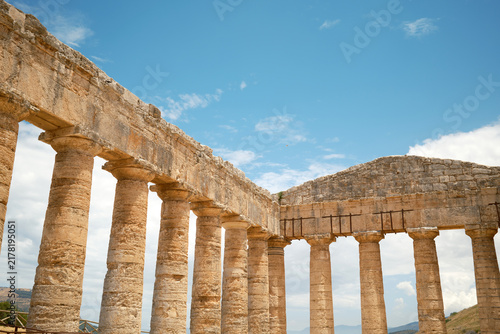 Wide low-angle interior shot of long Doric colonnade meeting end pediment under blue sky in Segesta, Sicily, Italy