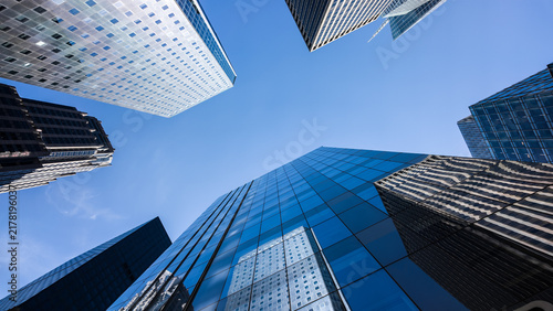 Картината върху платно Modern skyscrapers and glass office buildings in business district, captured from low angle perspective with blue sky, symbolizing architecture, urban growth, corporate success, and city development