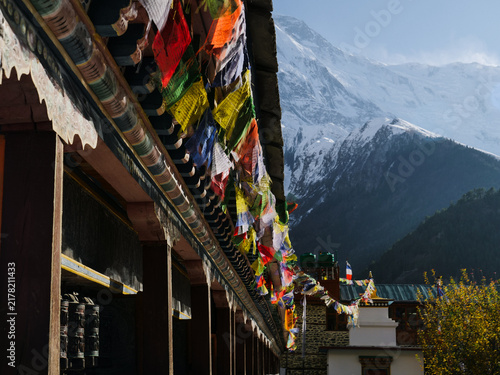 Fotografía Colorful Buddhist prayer flags adorn a traditional monastery building with a majestic snow-capped Himalayan mountain peak in the background, Nepal