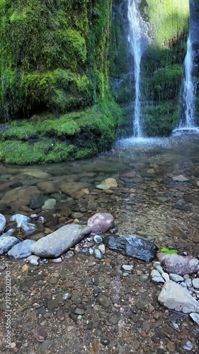 4K smooth stabilized footage of beautiful Spirit Falls in Oregon, USA, flowing gently over a lush moss-covered rock formation in an evergreen forest during the dry late summer season