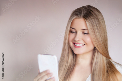 Quadro su tela Young woman smiling while looking at her smartphone, communicating and staying c