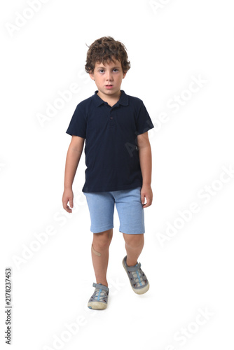 front view of a boy dressed in summer clothes walking and  looking at camera on white background (6 year old)